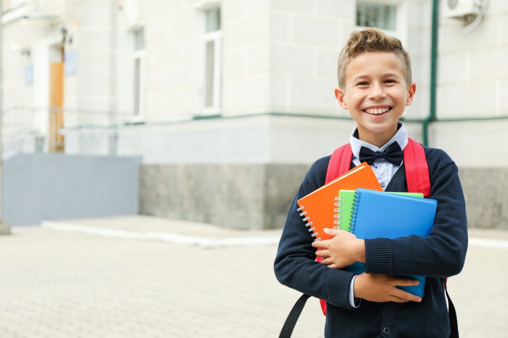 Boy with copybooks against school building, space for text