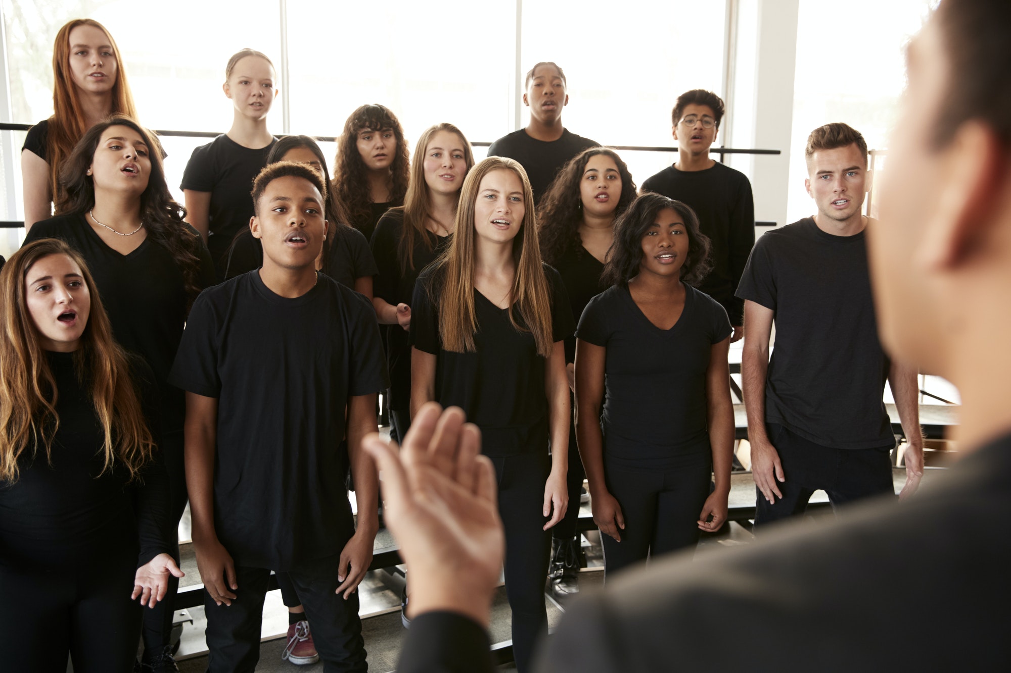 Male And Female Students Singing In Choir With Teacher At Performing Arts School