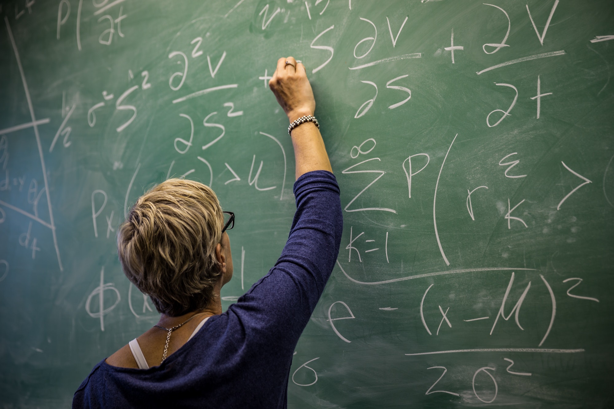 Master teacher at work teaching math on green chalkboard