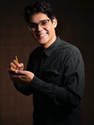 smiling man wearing black denim jacket holding pencil and sticky note while standing