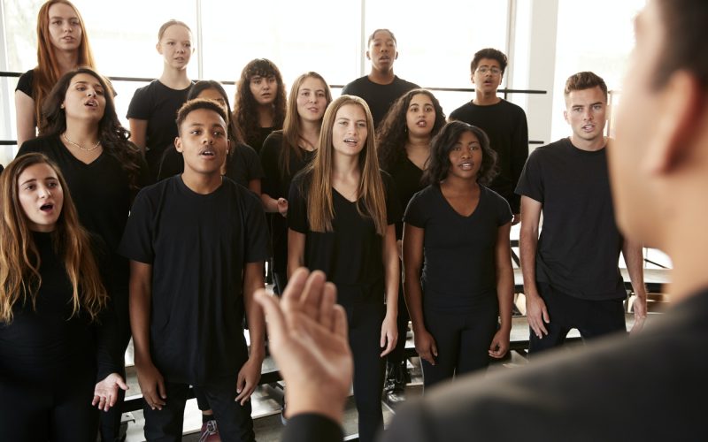 Male And Female Students Singing In Choir With Teacher At Performing Arts School