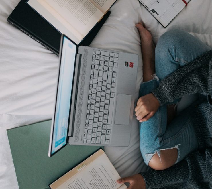 woman in blue long sleeve shirt and blue denim jeans sitting on bed using macbook