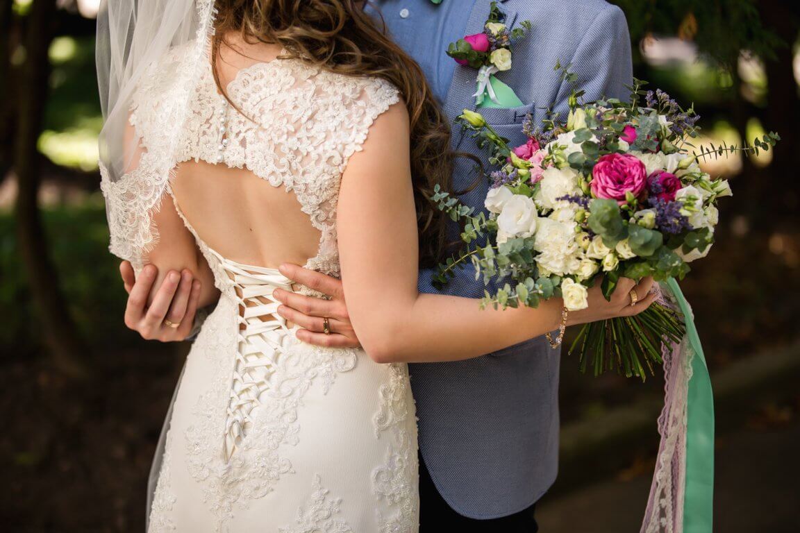 optimize- bride-groom-embracing-park-lace-back-bridal-dress-wedding-bouquet-hand-bride